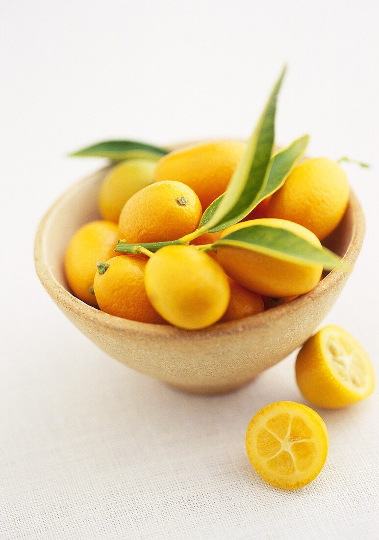 Kumquats in einer Schale mit zwei Hälften daneben