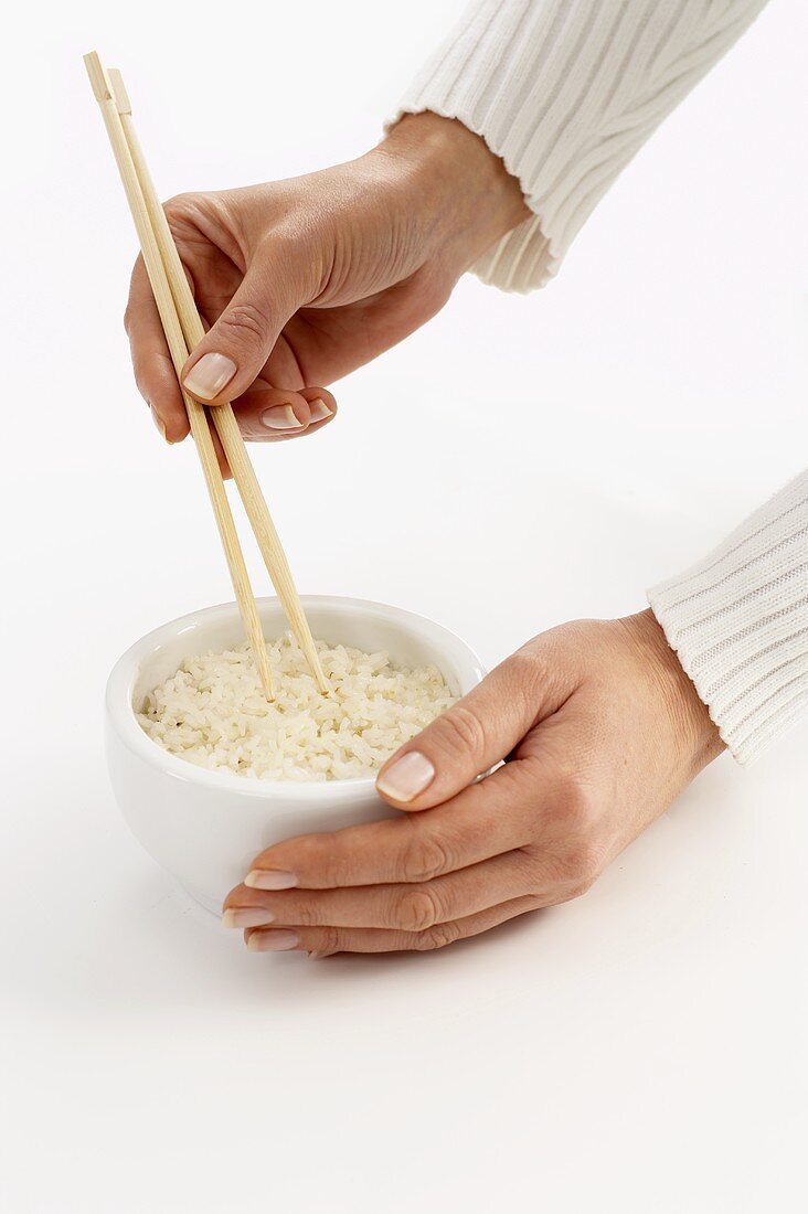 Frauenhände halten Stäbchen in eine Reisschüssel