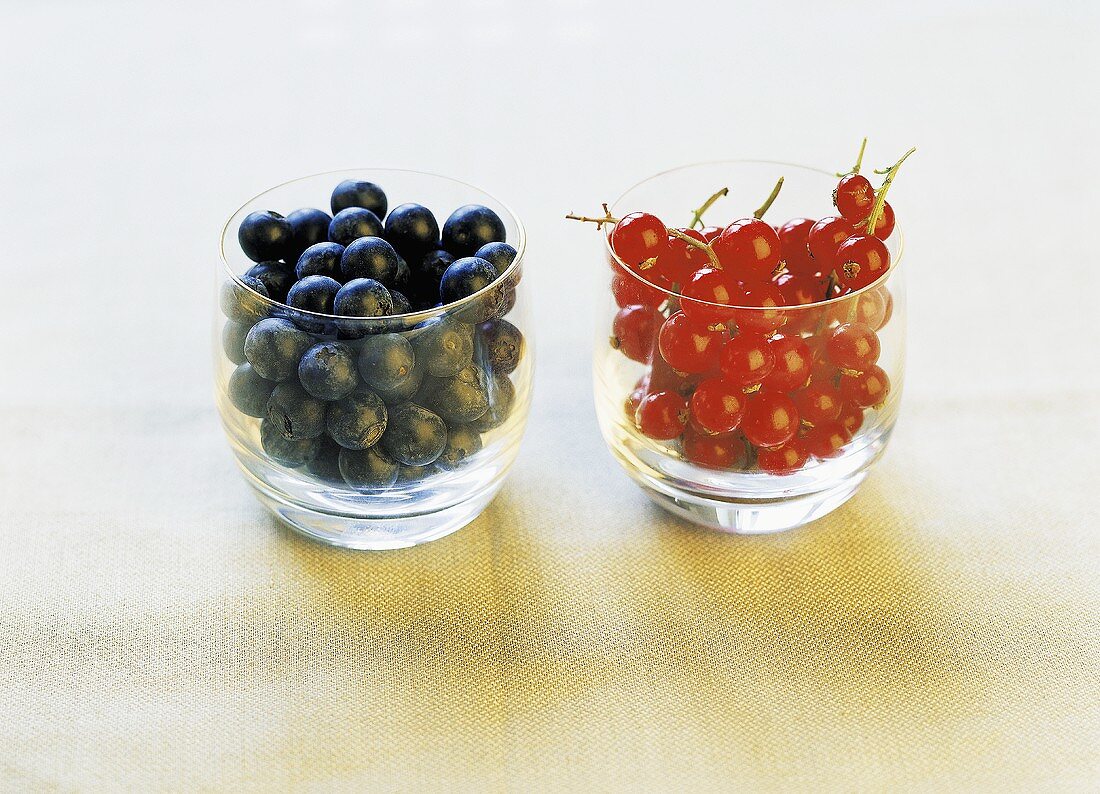 Blueberries and redcurrants in two separate glasses