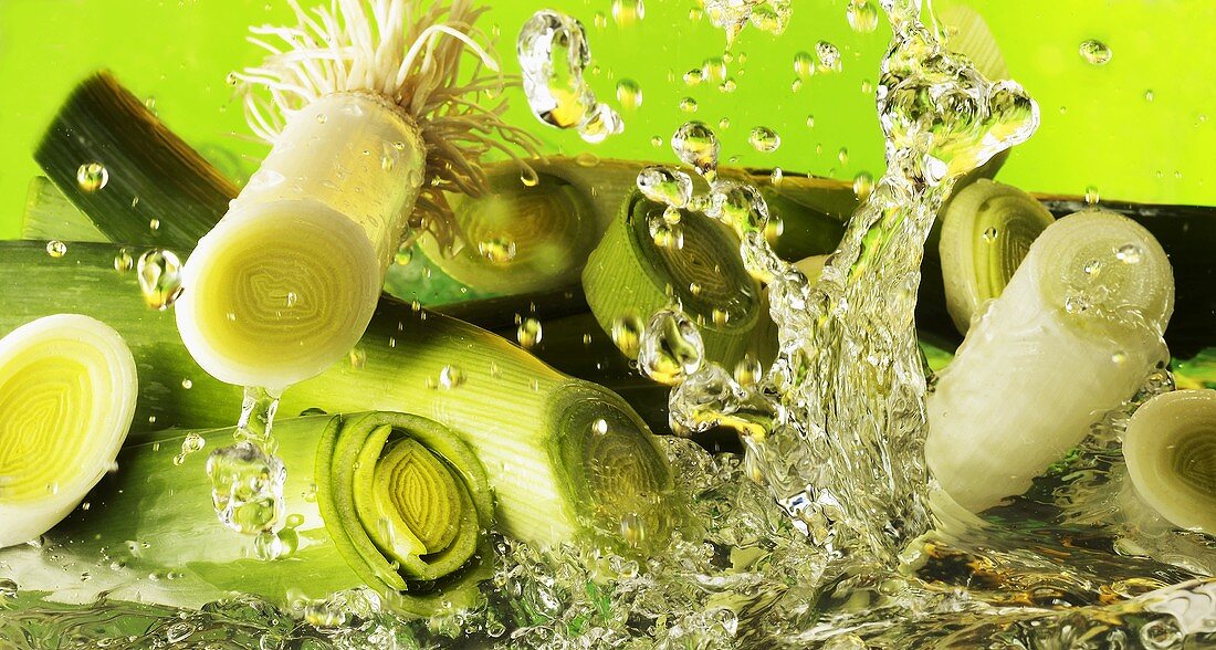 Pieces of leek falling into water against green background