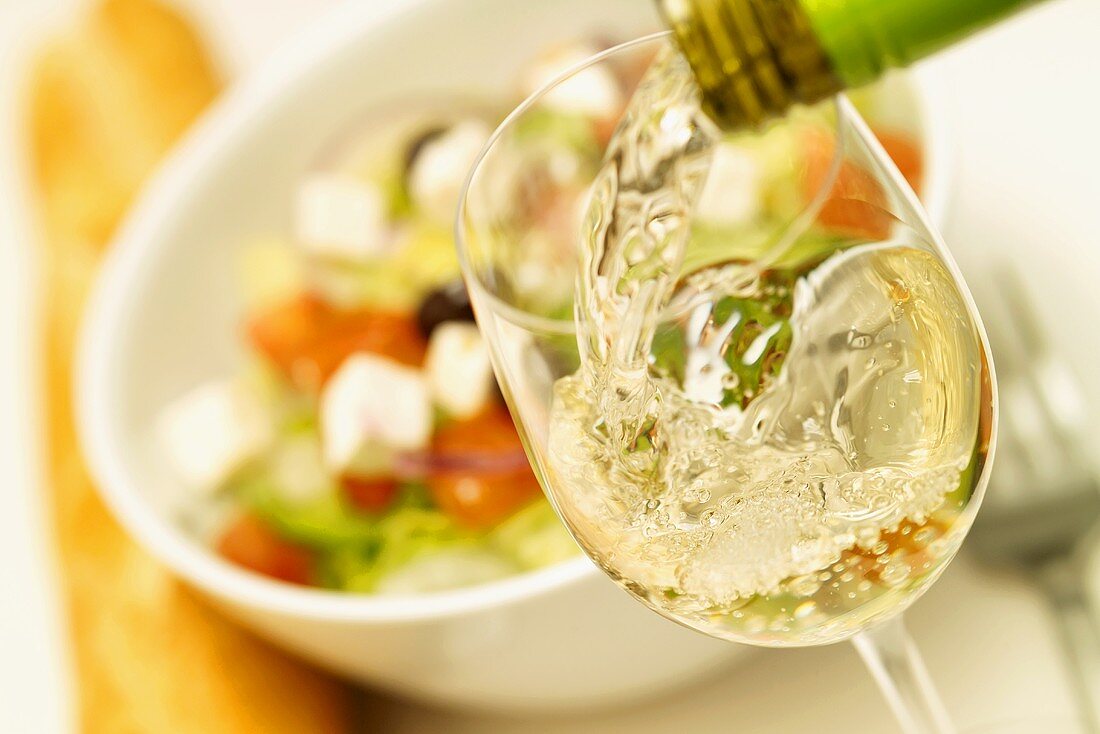White wine being poured into white wine glass, salad behind