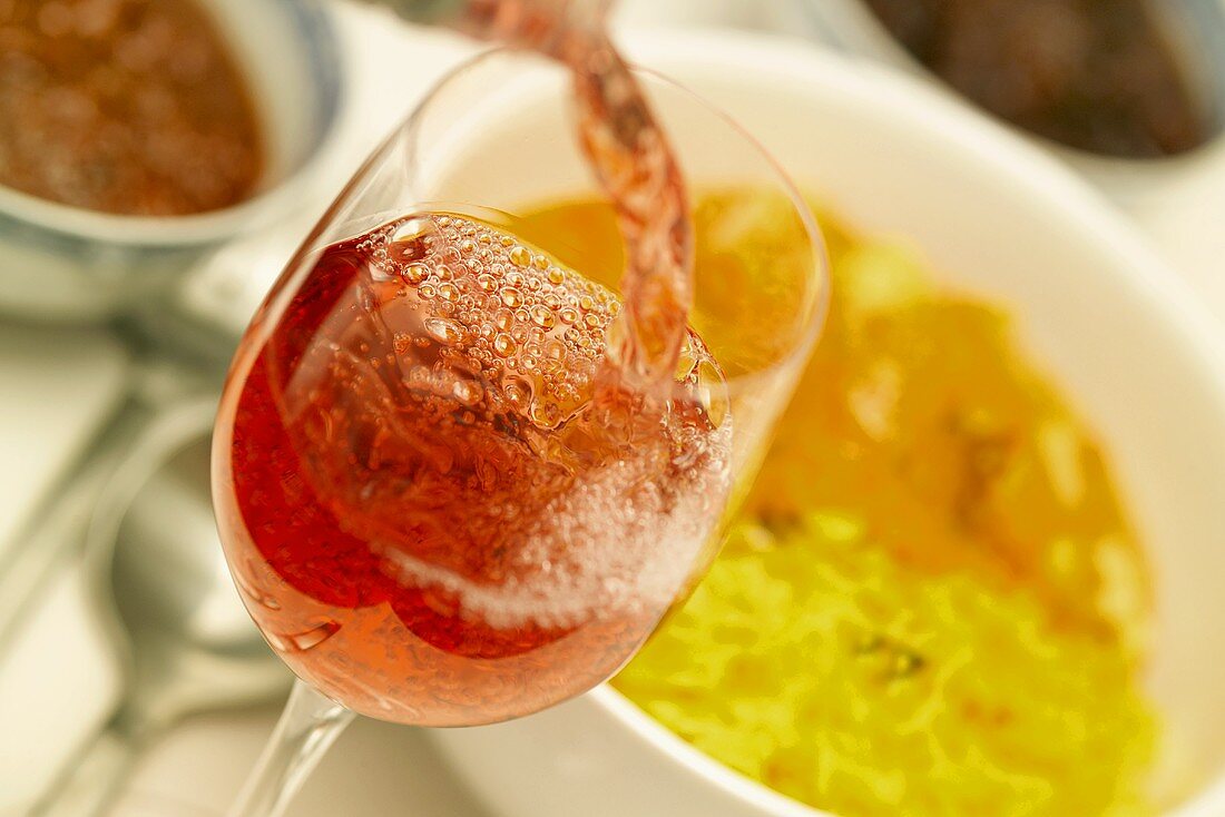 Rosé wine being poured into a glass, curried chicken behind