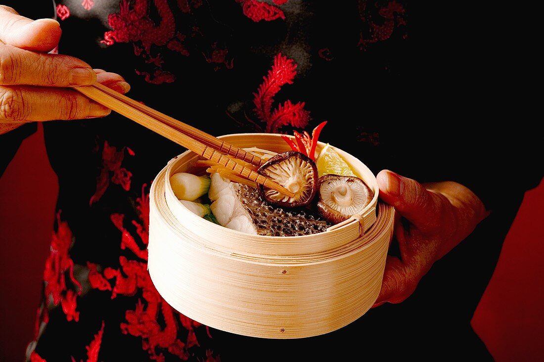 Woman taking food from steaming basket with chopsticks