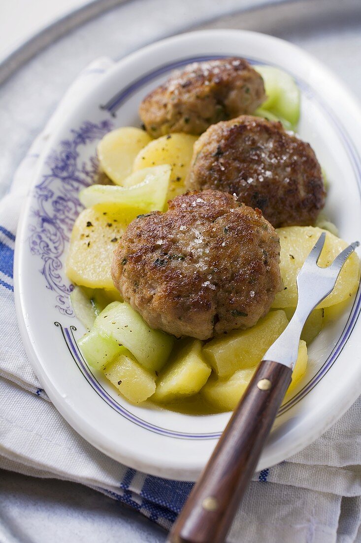 Fleischpflanzerl auf Kartoffel-Gurken-Salat und Fleischgabel