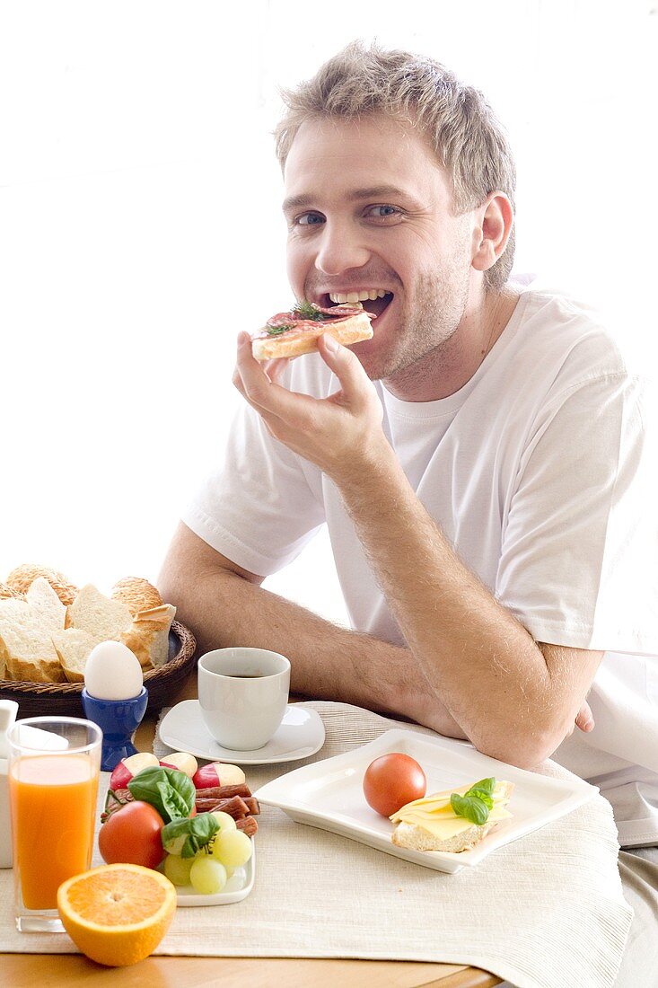 Young man biting into an open salami sandwich