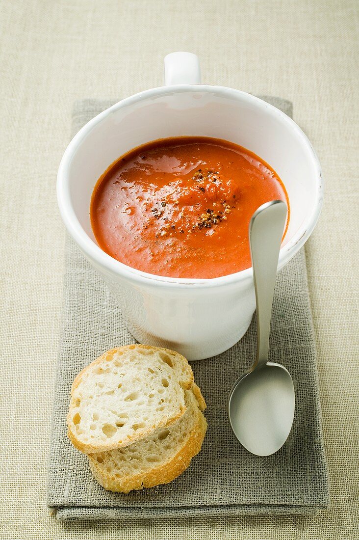 Creamed pepper soup in soup cup, spoon and baguette slices