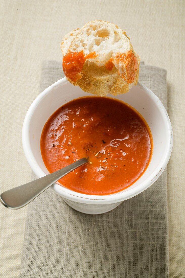 Red pepper cream soup in soup cup, spoon & baguette slices