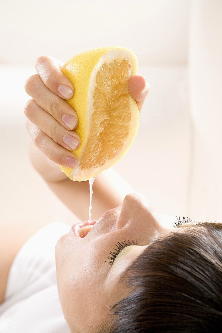 Junge Frau presst eine Grapefruit über ihrem Mund aus