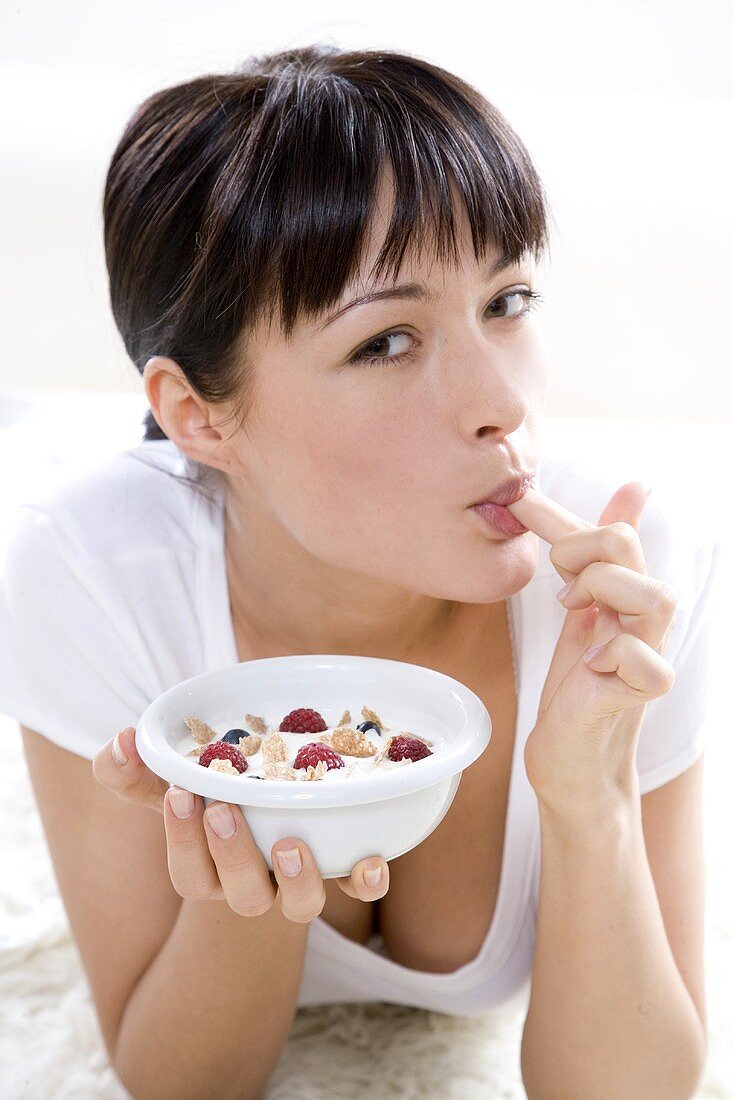 Young woman holding a bowl of muesli & licking her finger