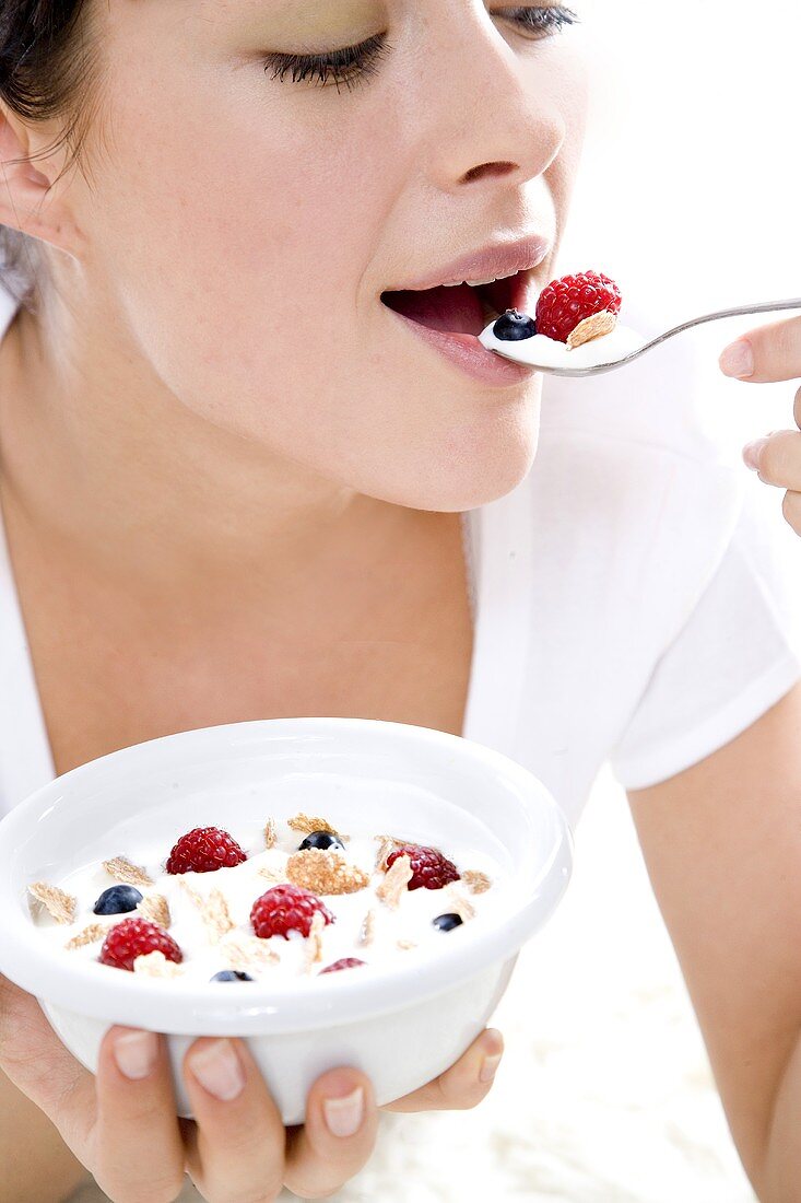 Young woman eating muesli with fresh berries and yoghurt