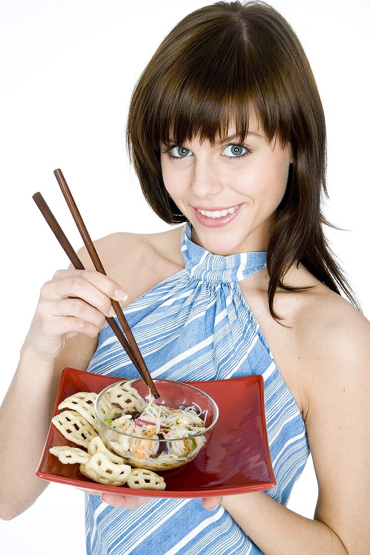 Junge Frau hält asiatisches Nudelgericht mit Essstäbchen