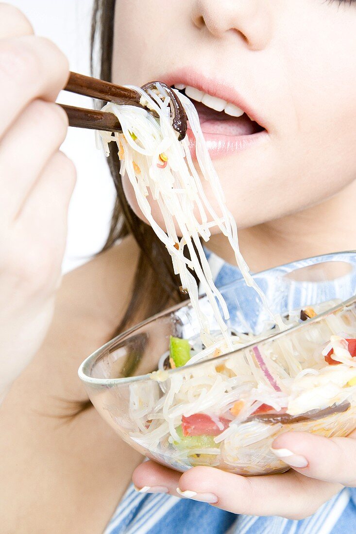 Young woman eating Asian noodle dish (detail)
