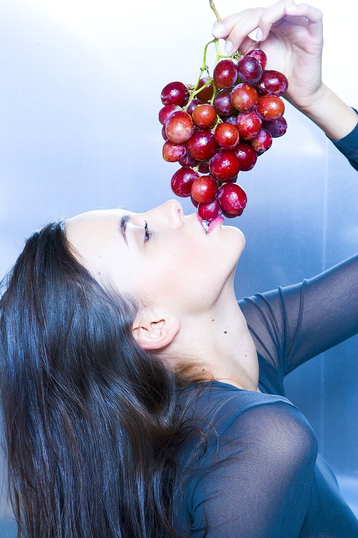 Woman holding red grapes over her mouth