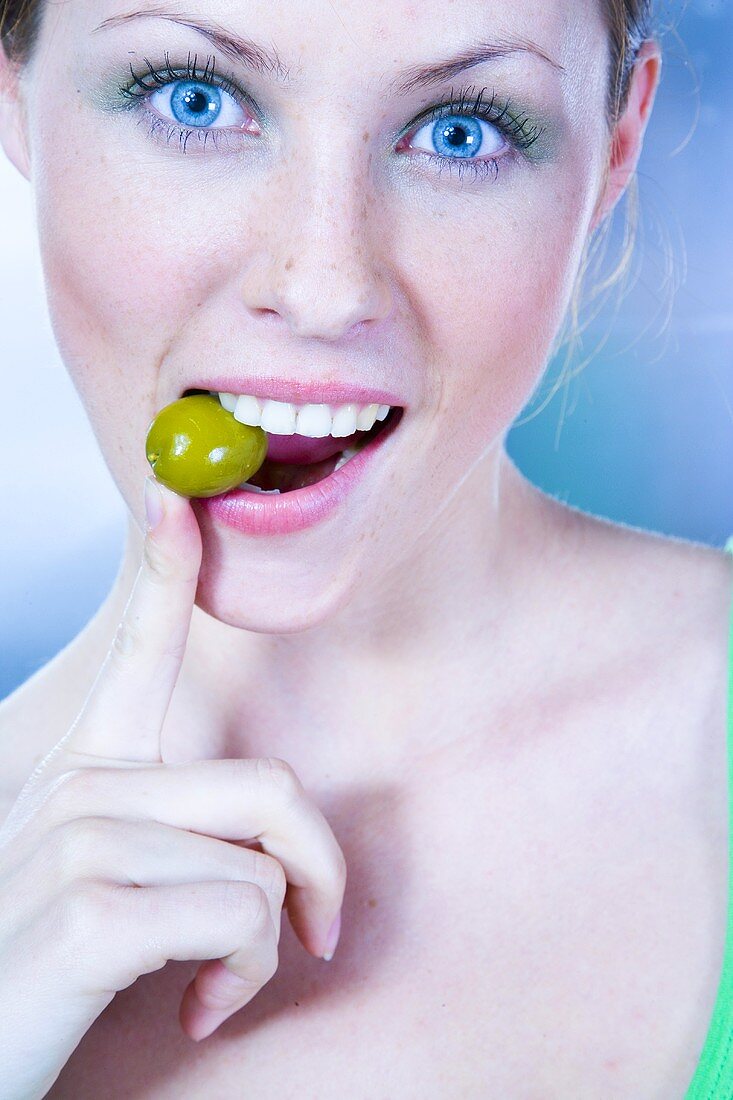 Junge Frau mit einer grünen Olive im Mund