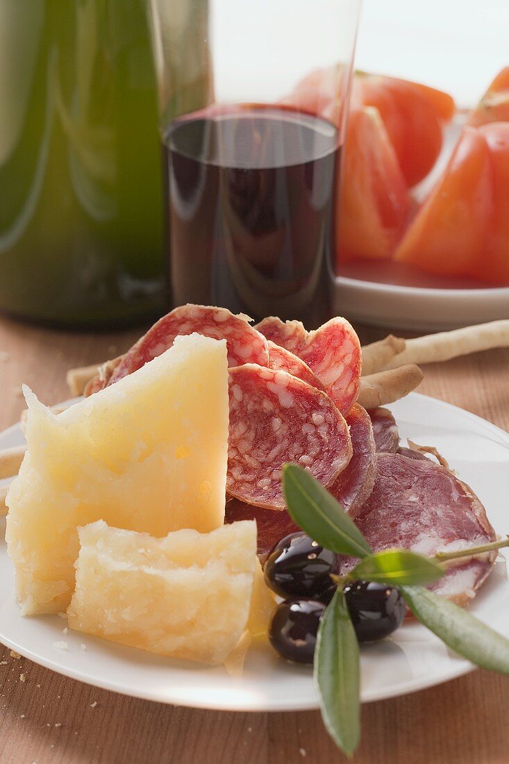 Salami, cheese, olives & grissini on plate, tomatoes, wine