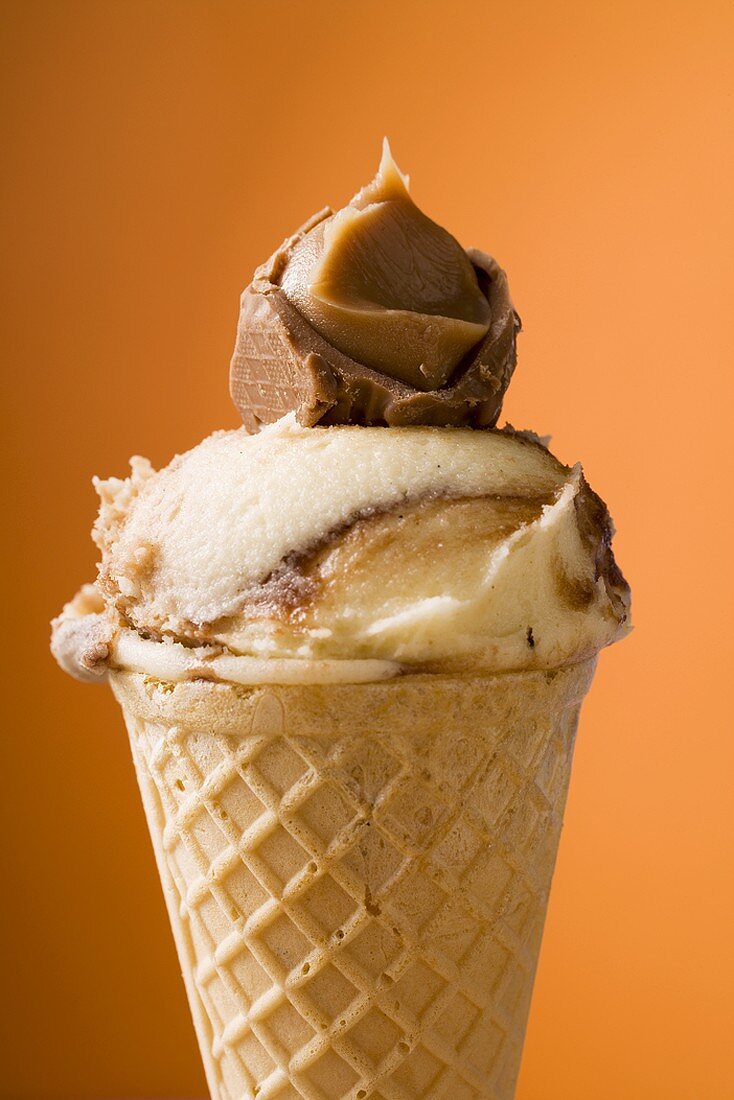 Caramel ice cream in wafer cone against orange background