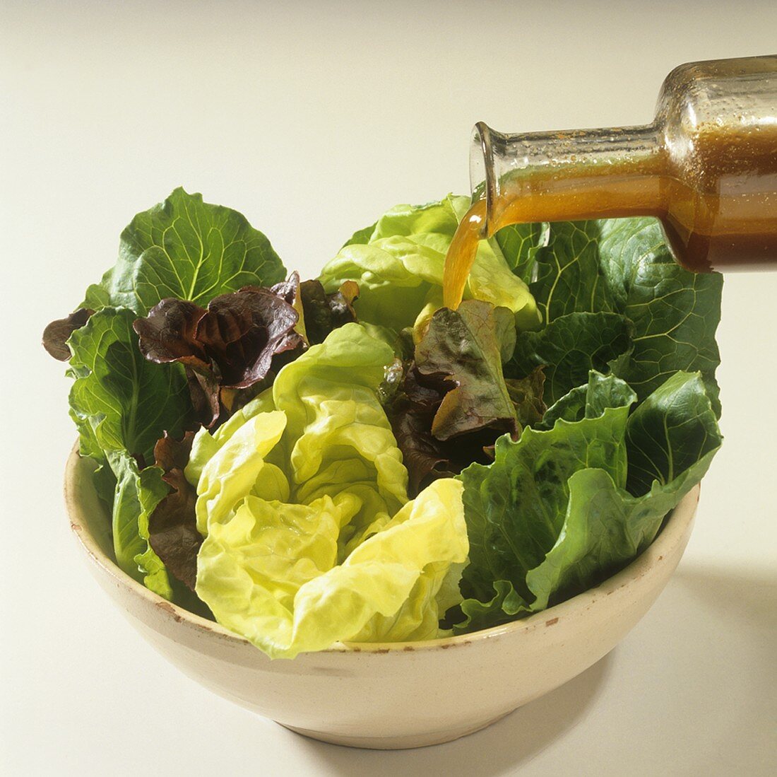 Pouring dressing over mixed lettuce leaves