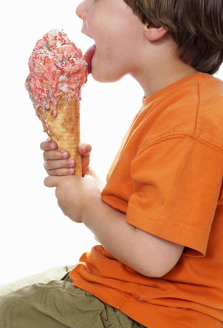 Boy licking a large strawberry ice cream with sprinkles