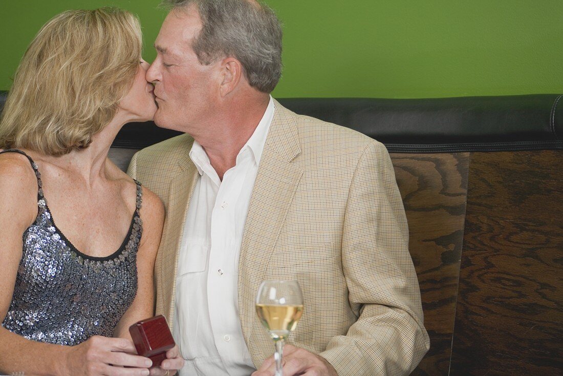 Älterer Mann küsst reifere Frau im Restaurant