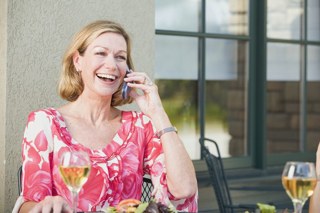 Blonde Frau an gedecktem Terrassentisch beim Telefonieren