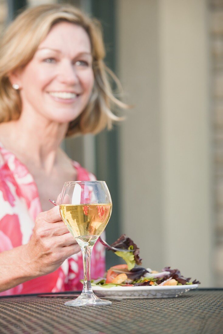 Blonde Frau am Tisch mit Salat und Wein