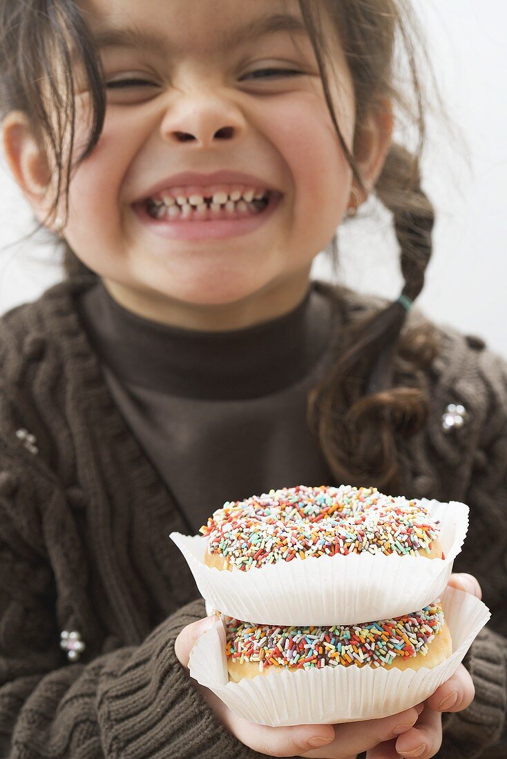 Giggling girl holding two doughnuts with sprinkles