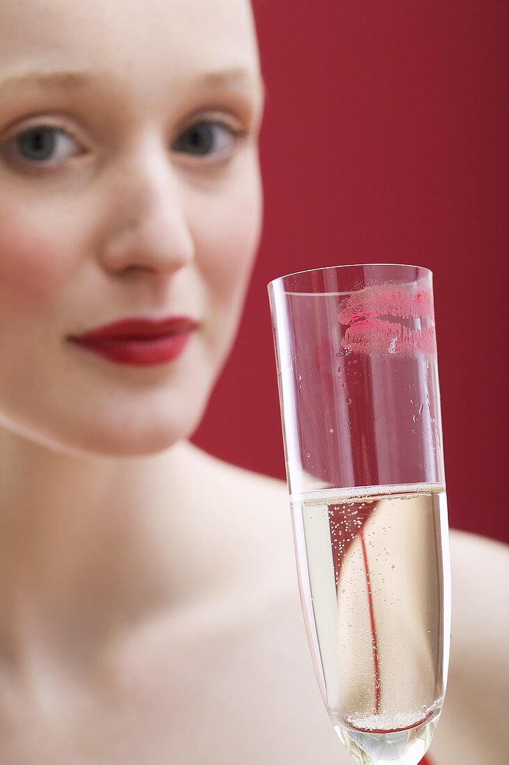 Junge Frau hält Sektglas mit Lippenstift-Abdruck
