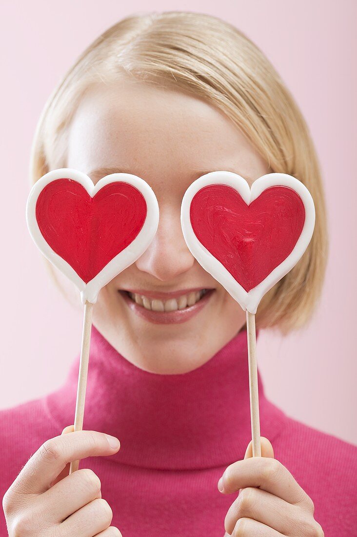 Love is blind: woman with heart-shaped lollipops in front of her eyes