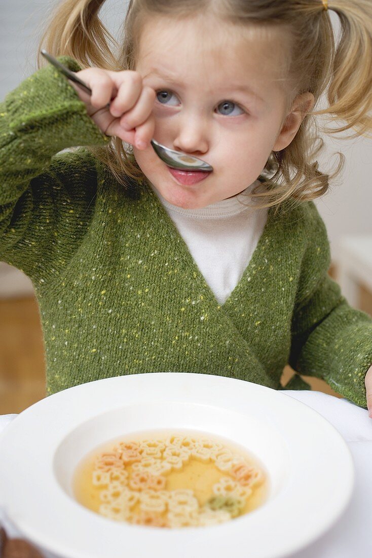 Small girl eating soup with teddy bear pasta