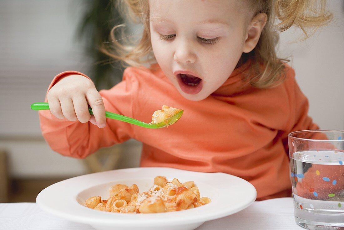 Small girl eating pasta with tomato sauce and Parmesan