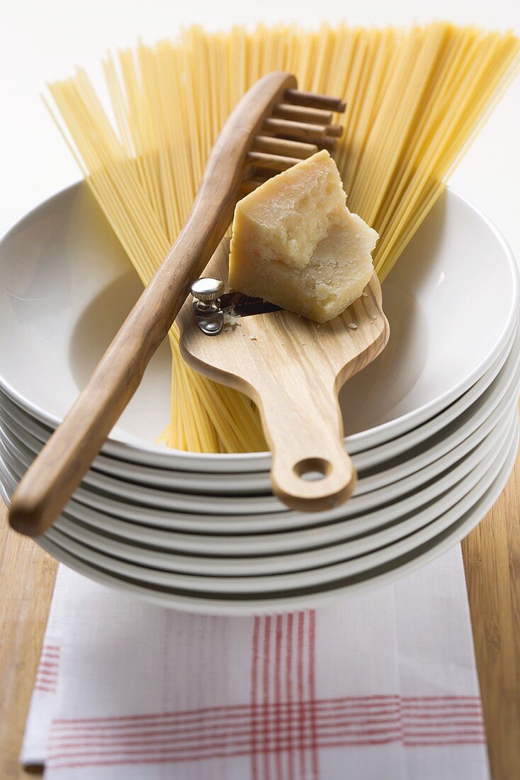 Spaghetti with spaghetti server & Parmesan on pile of plates