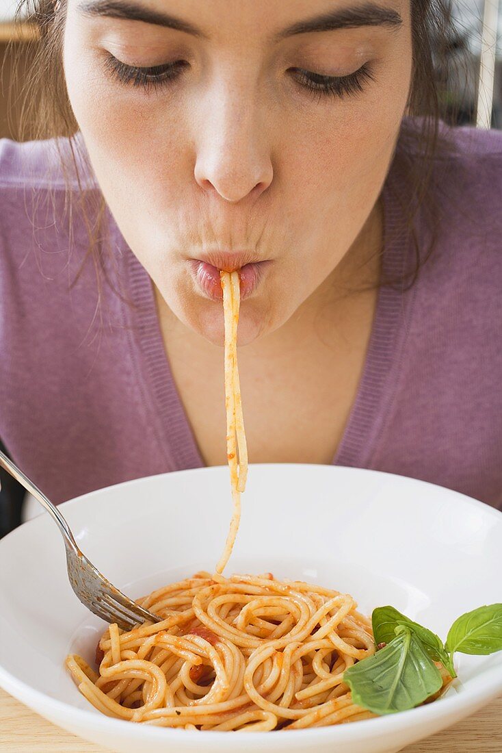 Young woman eating spaghetti with tomato sauce