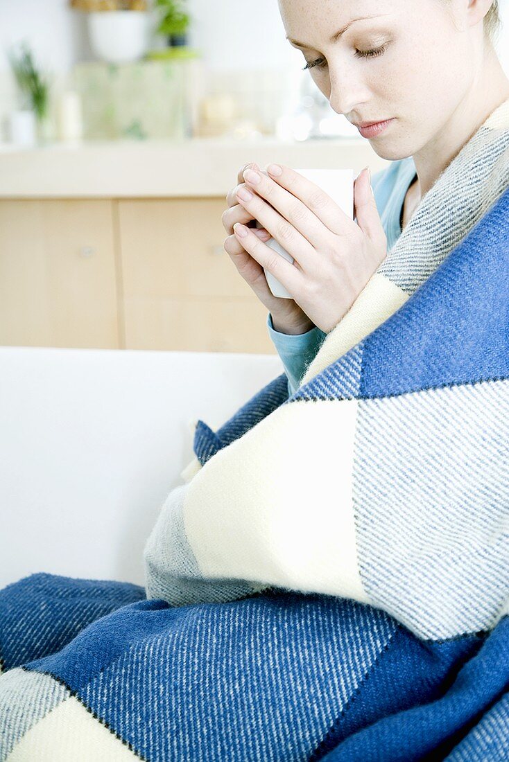 Junge Frau sitzt mit einer Tasse Kaffee auf dem Sofa