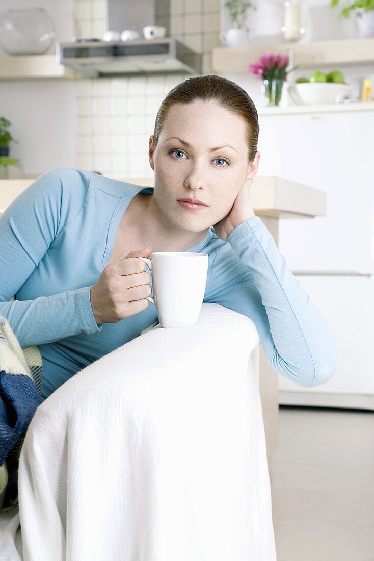 Junge Frau sitzt mit einer Tasse auf dem Sofa