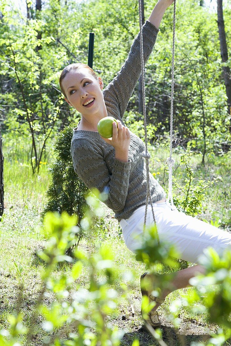 Junge Frau sitzt auf einer Schaukel mit einem Apfel