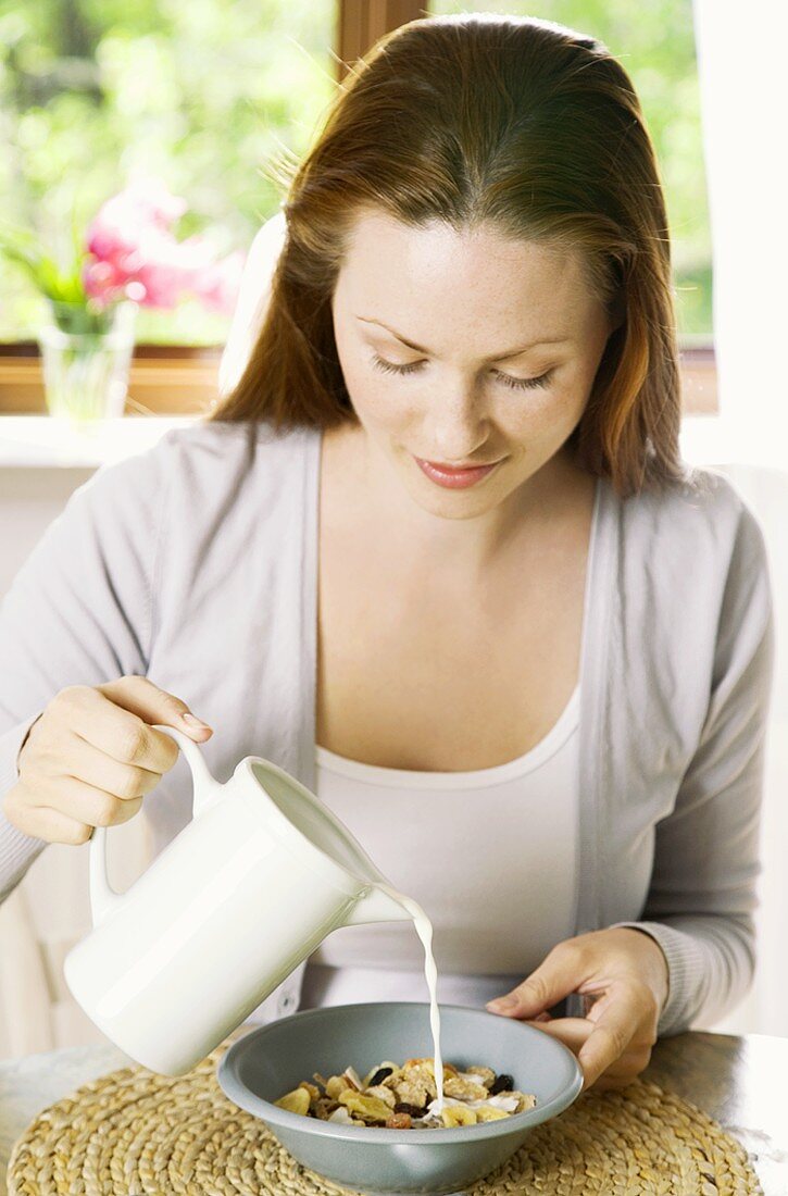 Junge Frau giesst Milch über Cornflakes