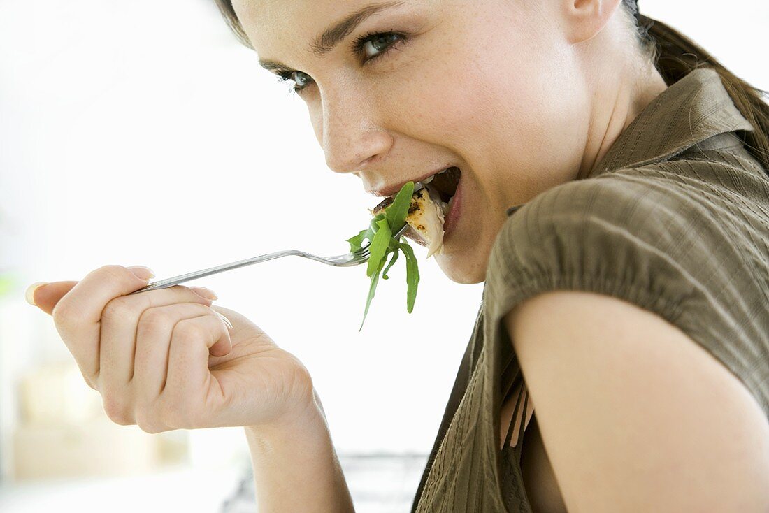 Young woman eating chicken breast with rocket