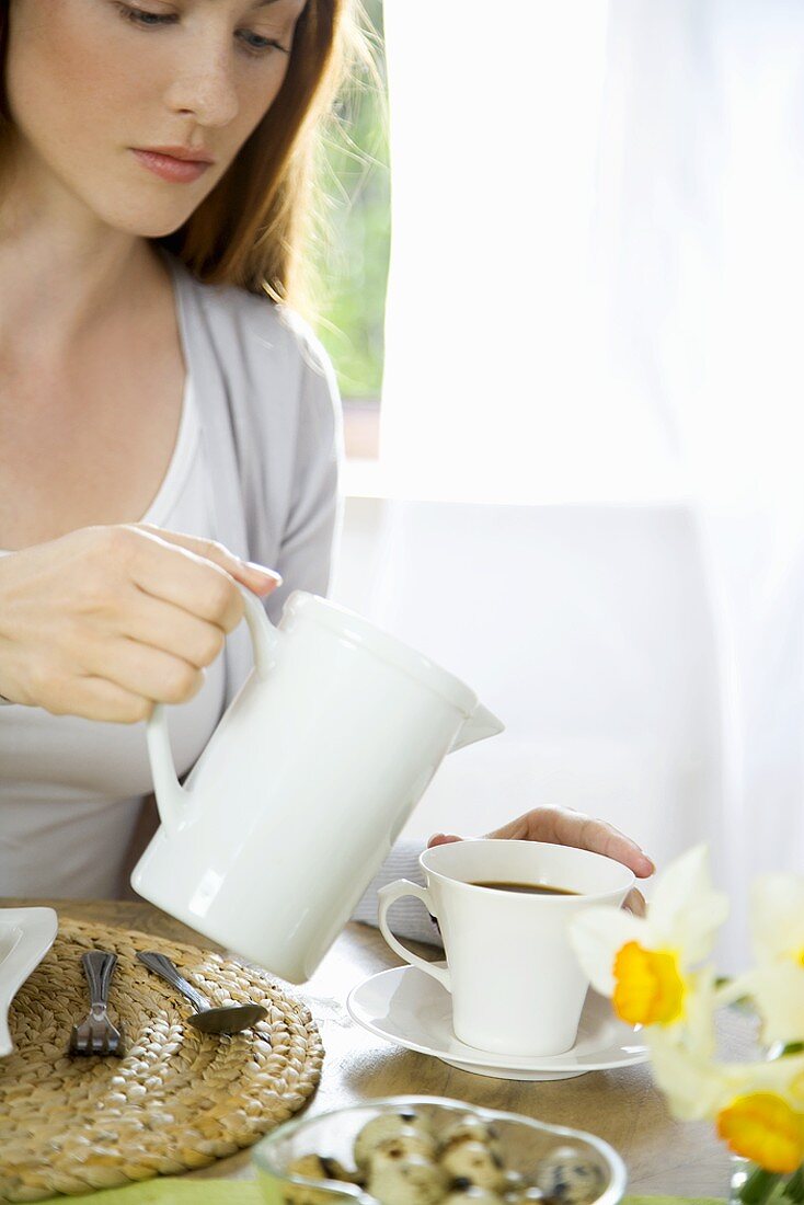 Young woman pouring milk into coffee