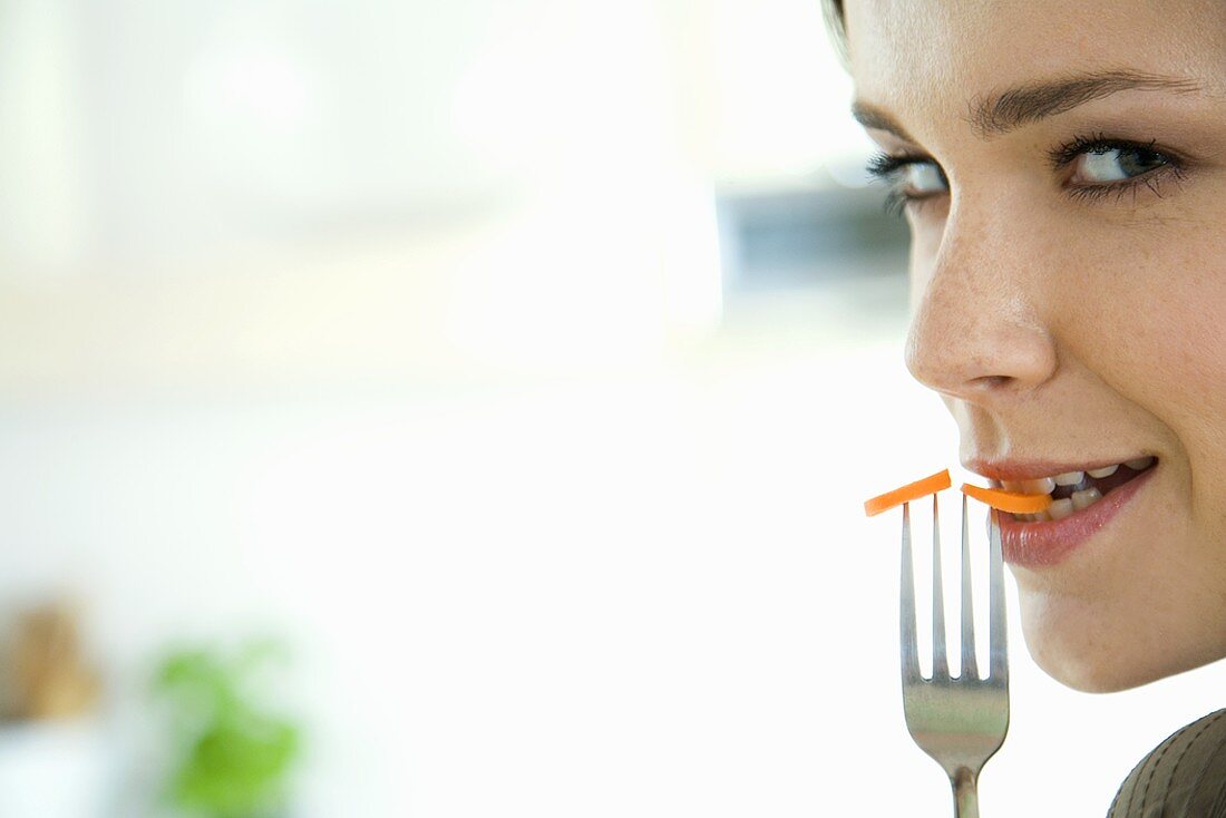 Young woman holding fork with carrot slices