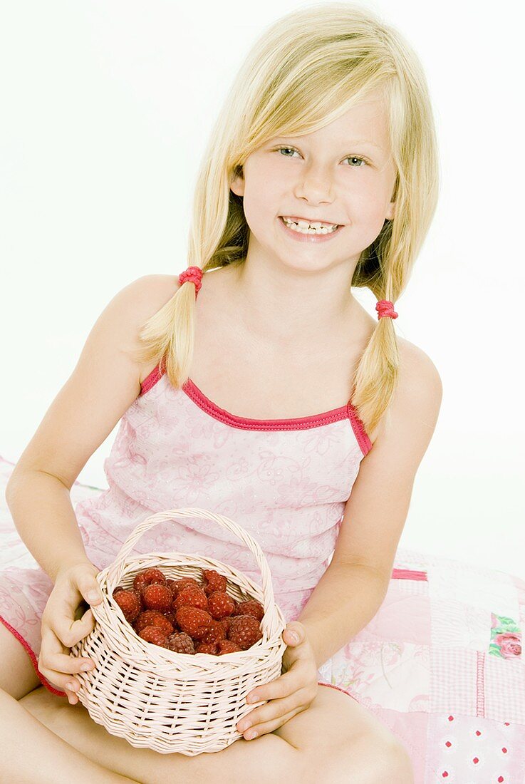 Blond girl holding small basket of fresh raspberries