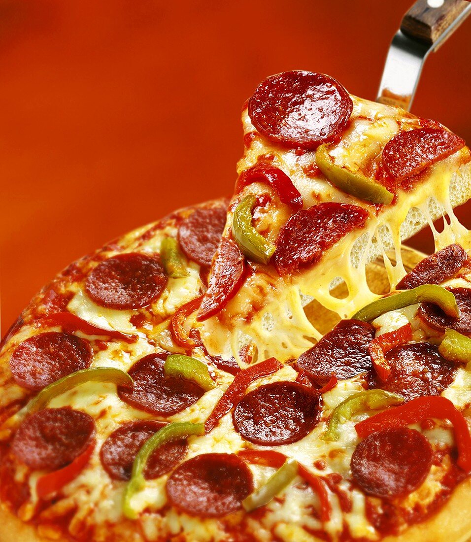 Pizza mit Salami und Peperoni, ein Stück auf Pizzaheber