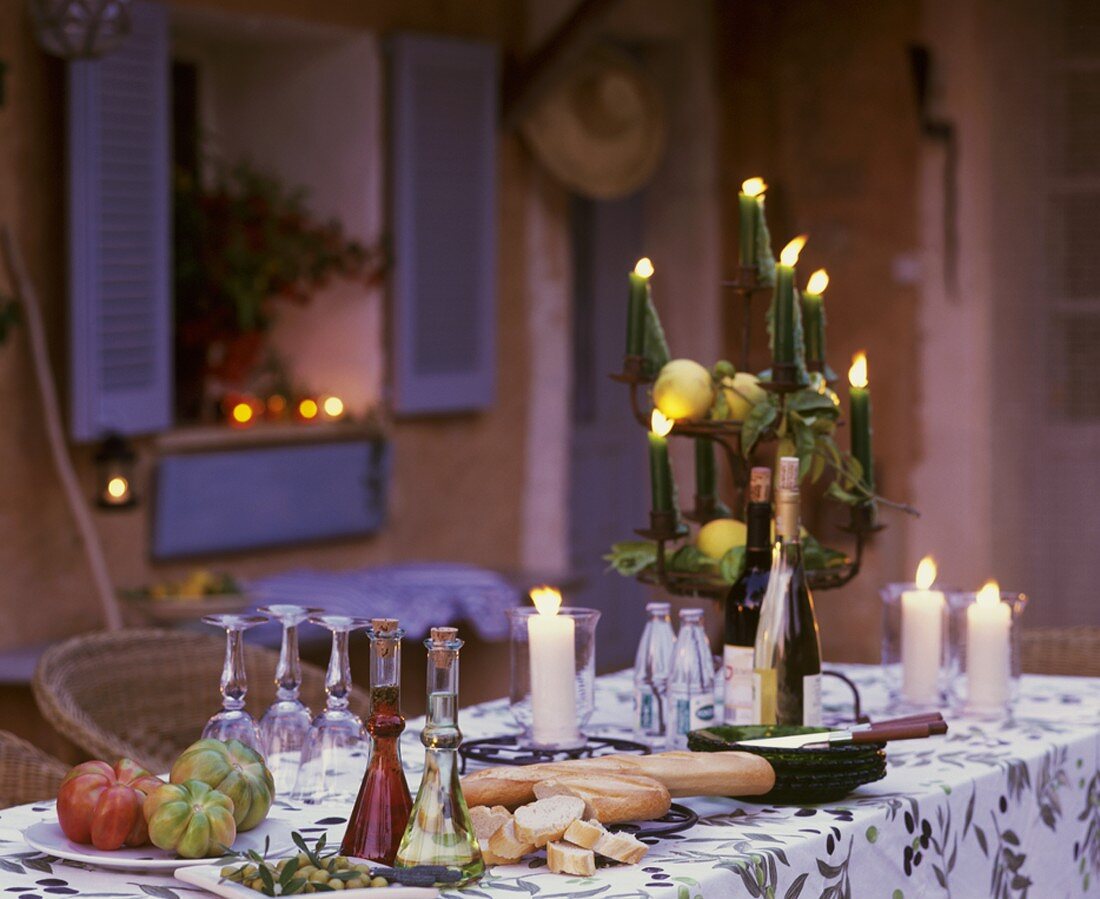 Tisch mit Tomaten, Baguette, Essig, Öl und Kerzen im Freien