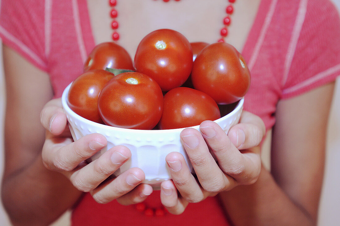 Hände halten weiße Schale mit Tomaten