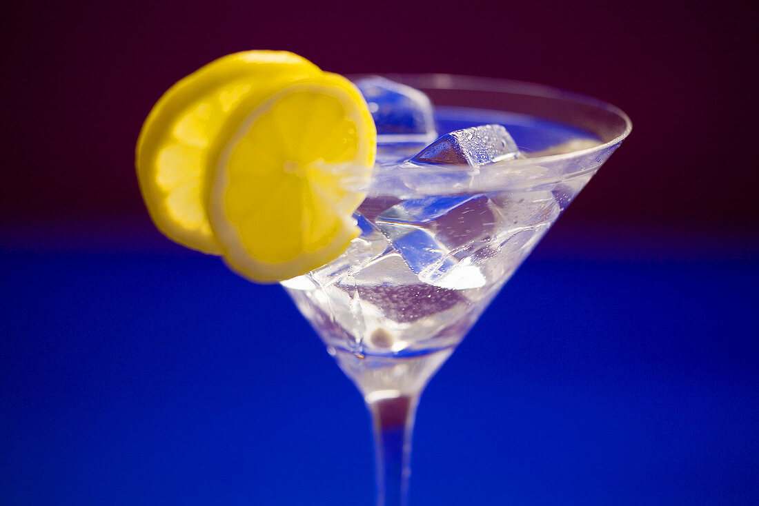 A glass of Martini with ice cubes and lemon slices