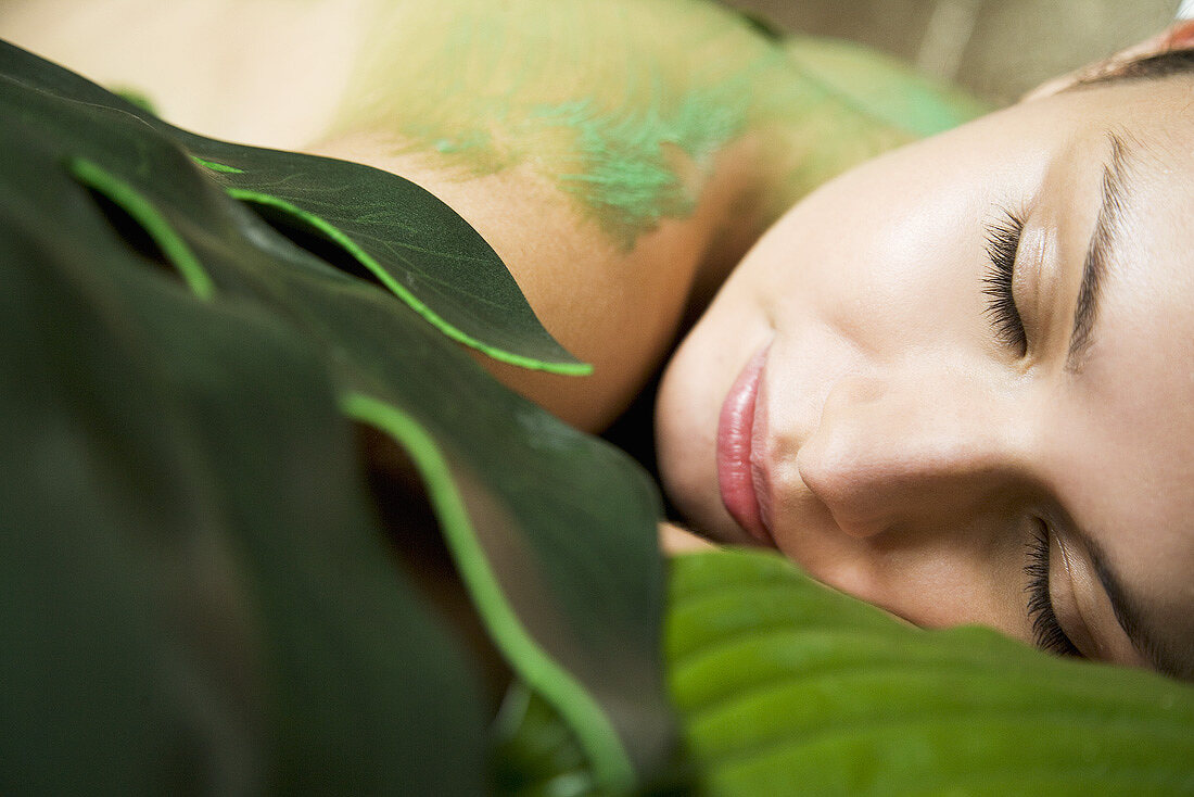 Young woman with body mask and leaves on her back