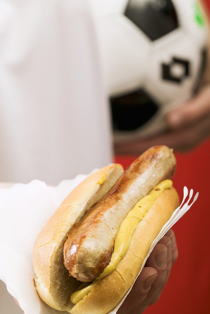 Footballer holding hot dog (sausage & mustard in bread roll)