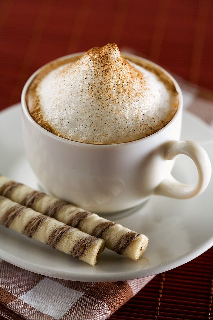 A cup of cappuccino with wafer rolls