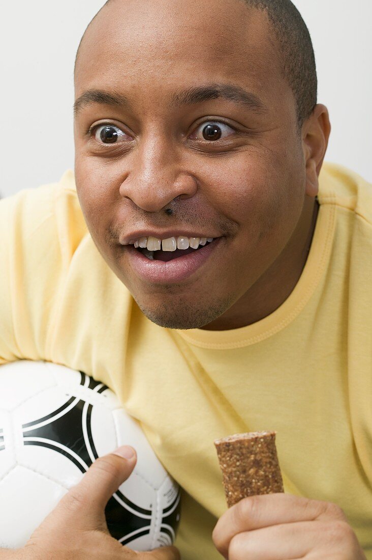 Junger Mann mit Fussball und Schokoriegel beim Fernsehen