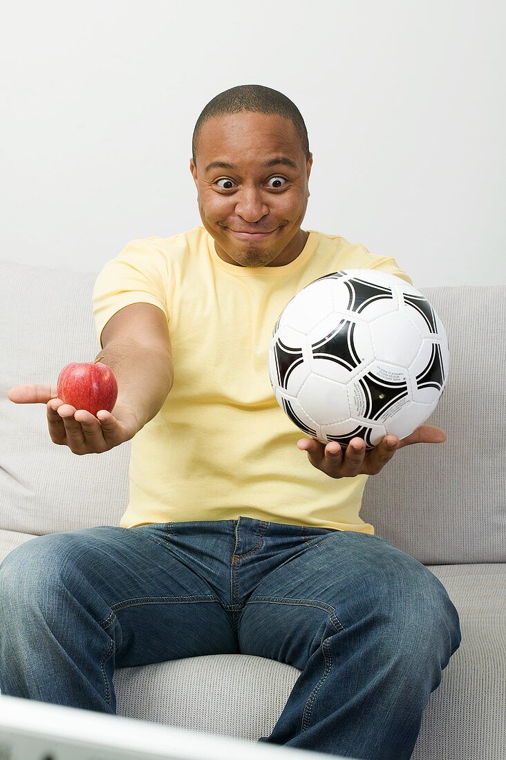 Junger Mann mit Apfel und Fussball beim Fernsehen