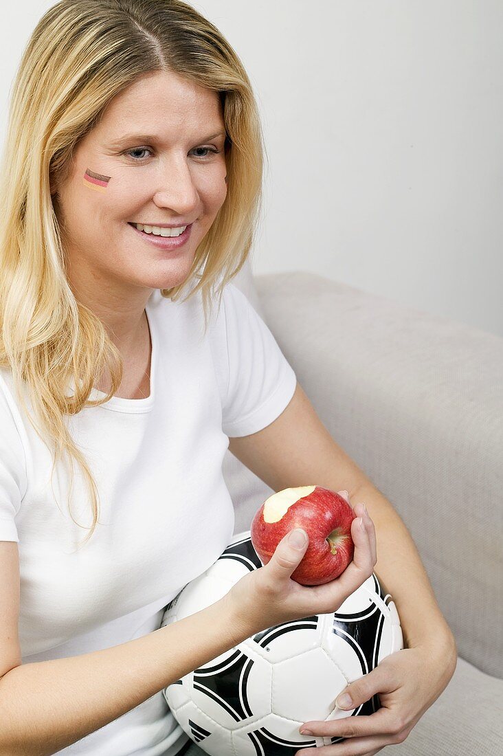 Junge Frau mit Fussball isst einen Apfel